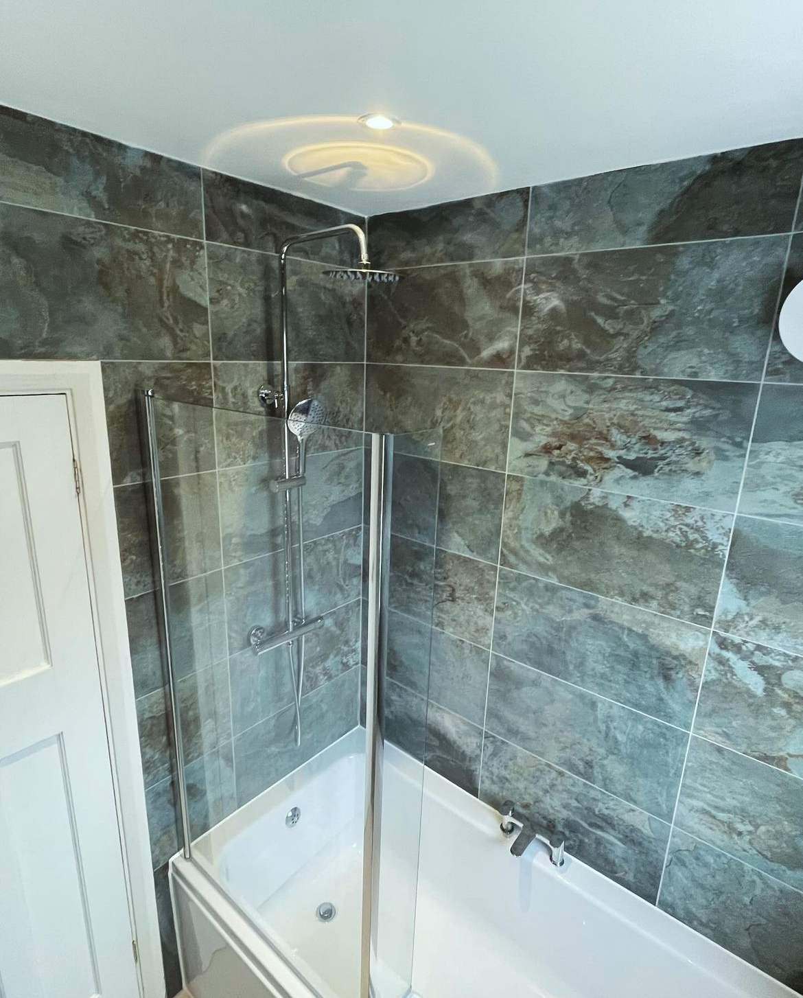Bath with rainfall shower over and glass screen against marbled tiling
