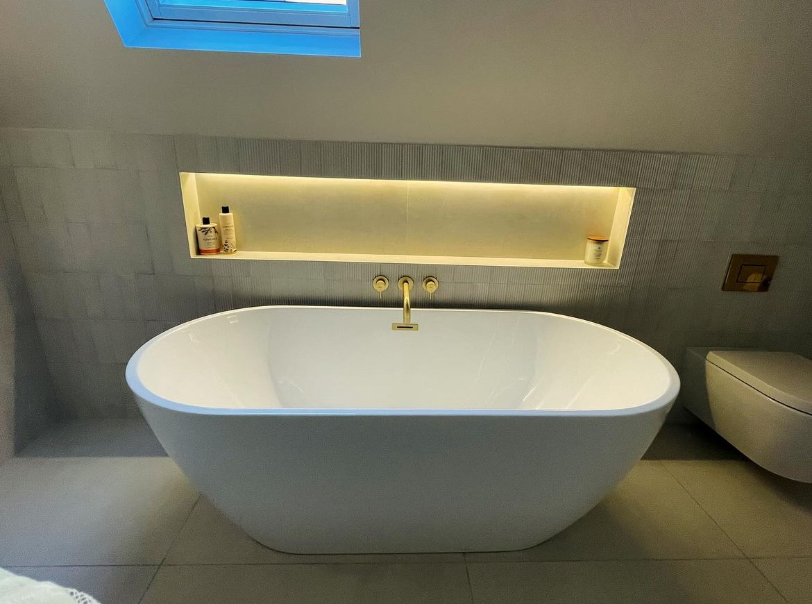 Freestanding bath with brushed brass wall mounted filler and lit niche