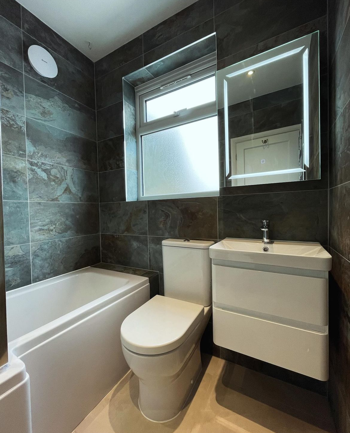 Slate tiled family bathroom with bath, WC and illuminated mirror