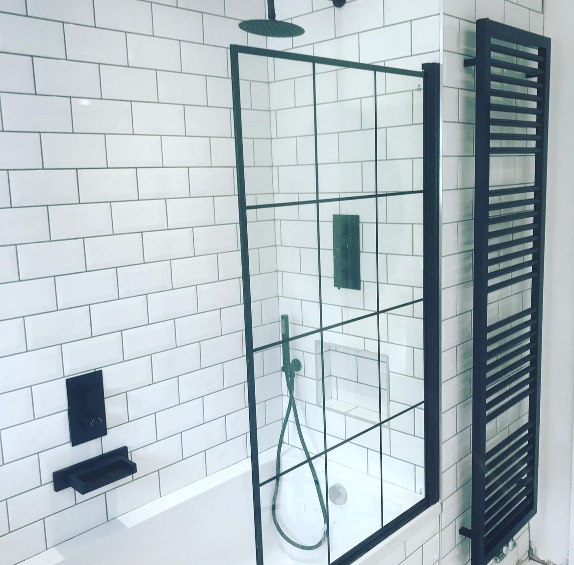 Metro tiled bathroom with crittall style bath screen and black towel radiator