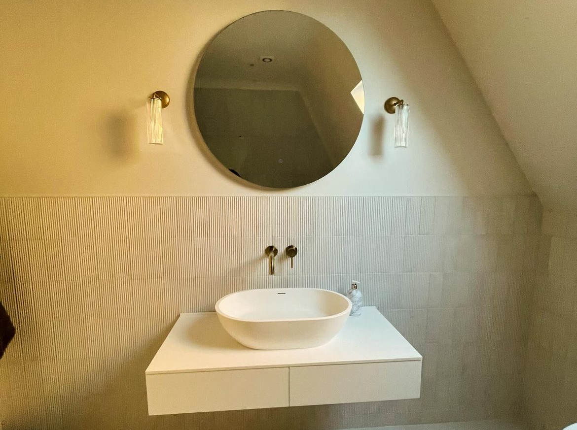 Countertop basin on a floating vanity with brass taps and round mirror